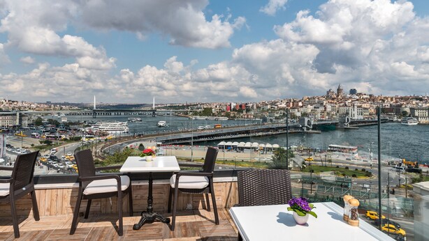 Una terraza con sillas de mimbre y una mesa, con vistas a un paisaje urbano que incluye un río y un puente.