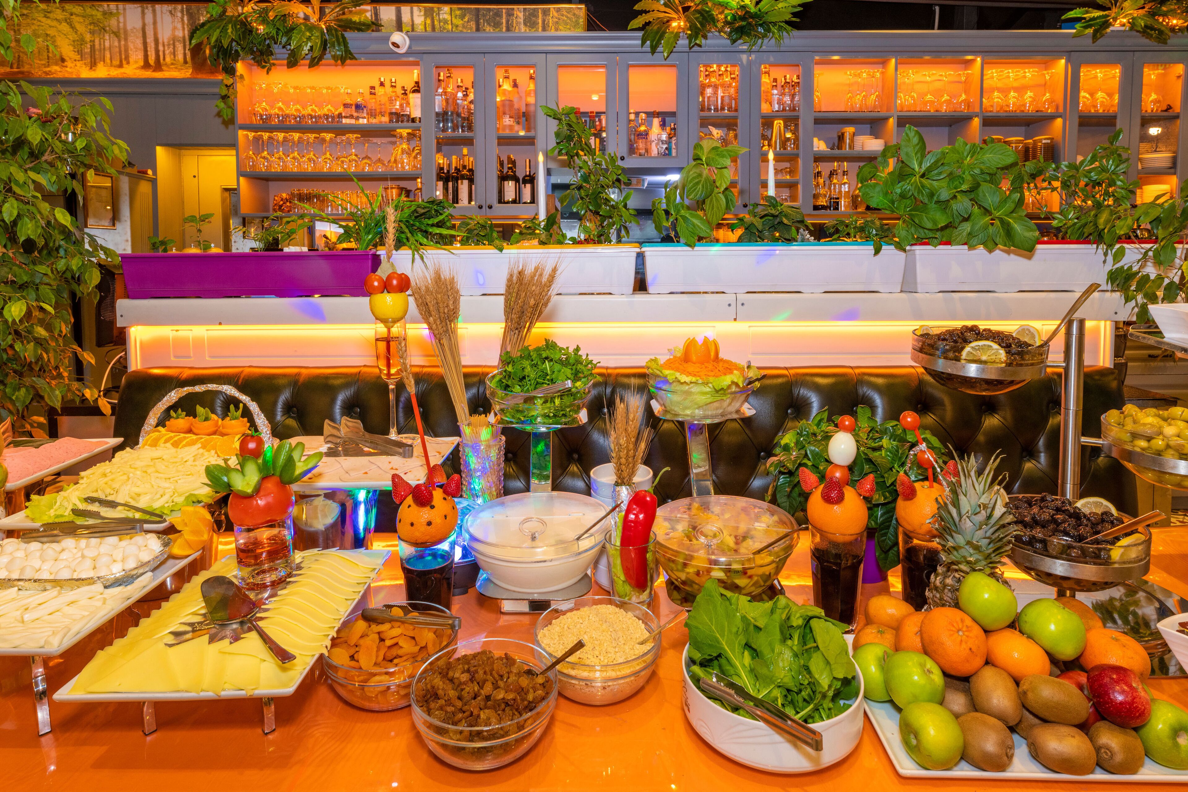 Un bufé con diversos alimentos y una zona de bar con estantes llenos de botellas y vasos.