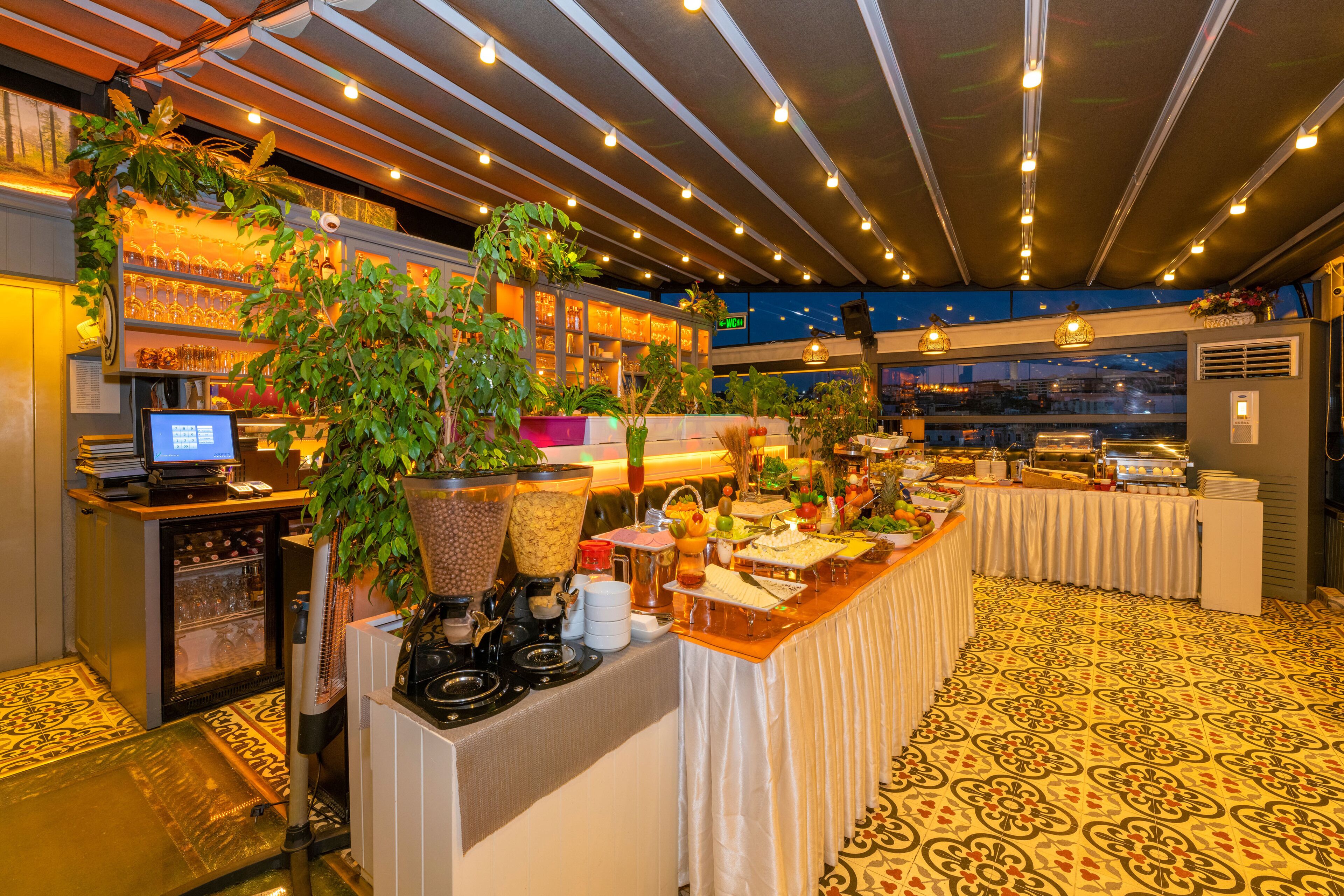 A buffet setup with a variety of food items, a coffee machine, and a seating area with a patterned floor.
