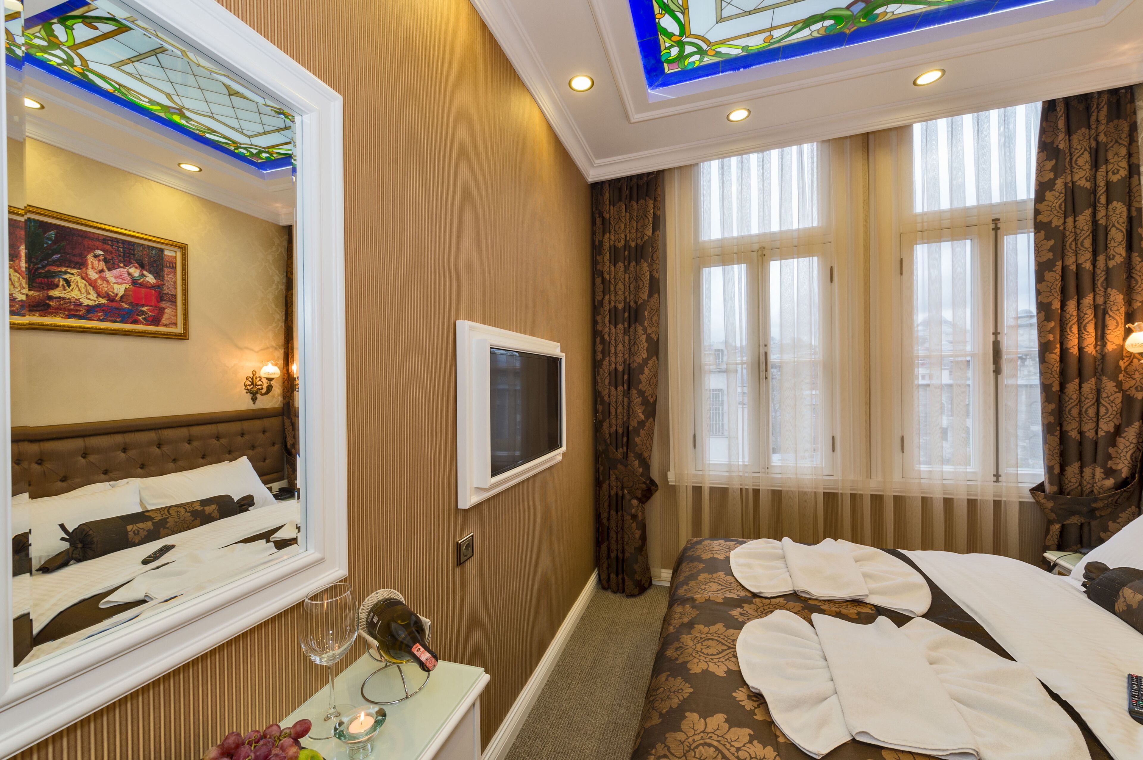 A hotel room with a large bed, a television, a mirror, and a painting on the wall.