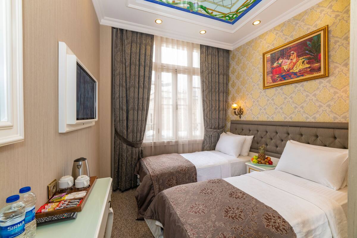 A hotel room with two beds, a TV, a minibar, and a painting on the wall.