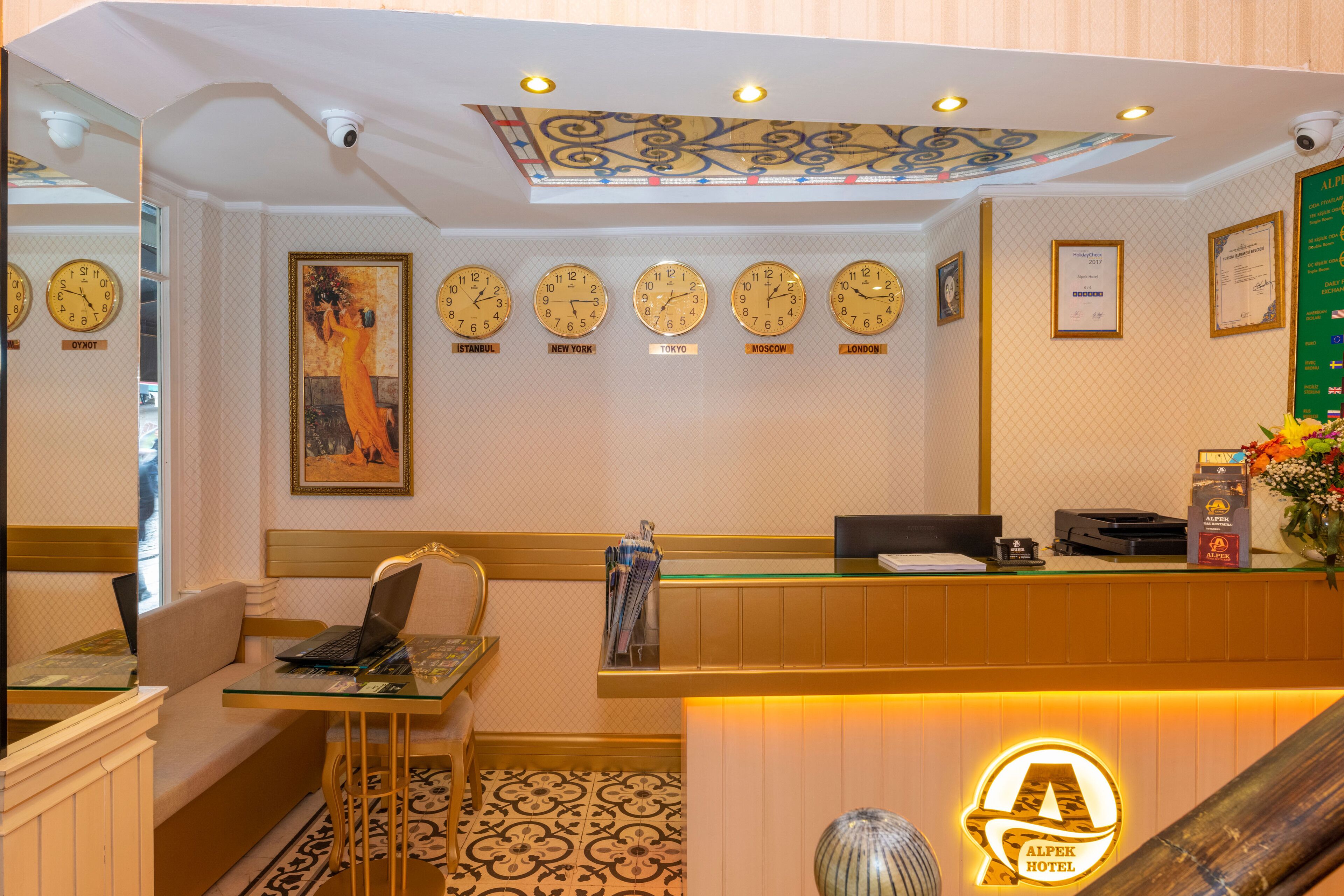 Un hall d’hôtel comprenant un comptoir d’accueil, des sièges, des horloges indiquant l’heure de différentes villes et un plafond décoratif.