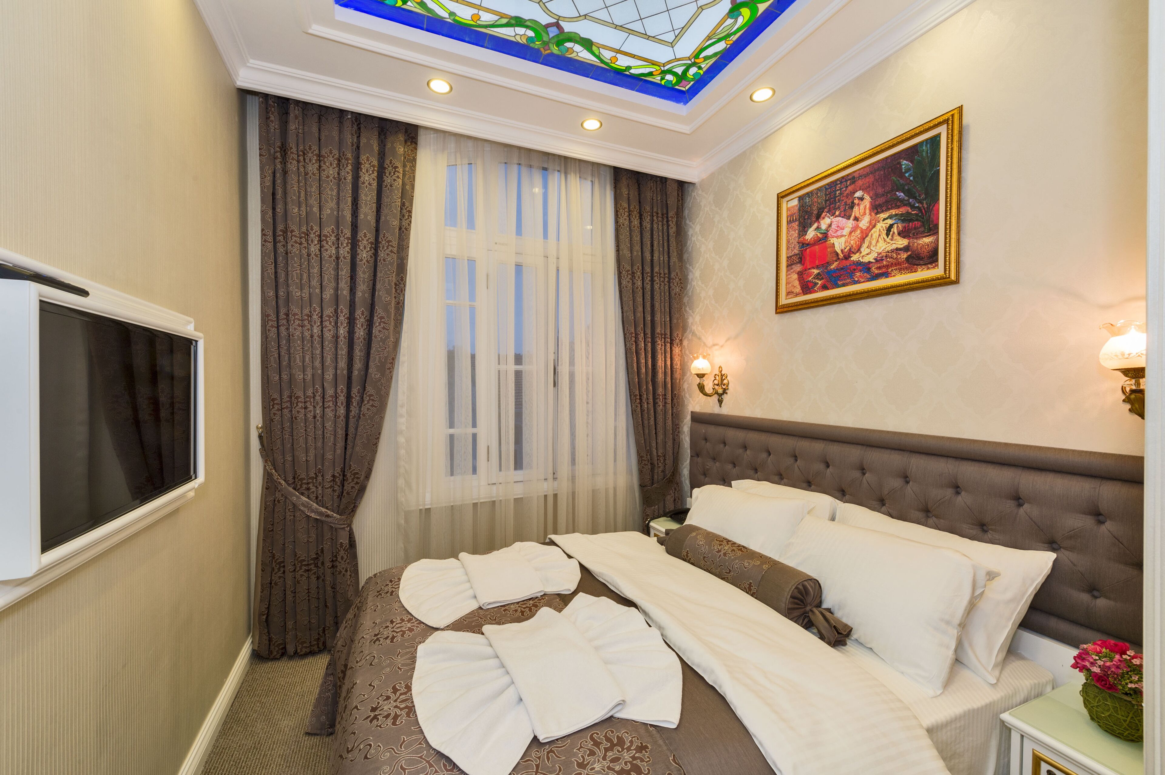 A hotel room with a large bed, a television, and a painting on the wall.