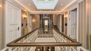 Un amplio pasillo con una escalera de madera, apliques ornamentales y un techo decorativo.