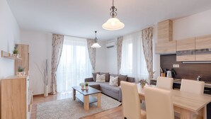 A modern apartment with a living room, dining area, and kitchen. There are two pendant lights, a sofa, a coffee table, and a dining table with chairs. - Fortuna 7 Apartments (Hévíz)