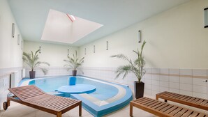 A modern indoor pool area with a blue pool, wooden loungers, and potted plants. - Fortuna 7 Apartments (Hévíz)