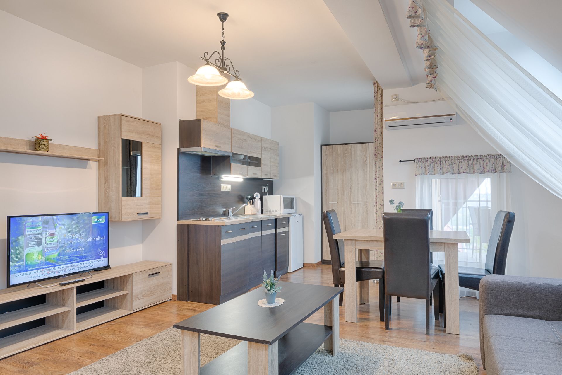 A modern kitchen with wooden cabinets, a dining area with a table and chairs, and a television on a wooden stand.