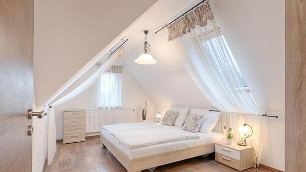 A bedroom with a sloped ceiling, a bed, a bedside table with a lamp, and a radiator. - Fortuna 7 Apartments (Hévíz)