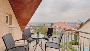 A balcony with wicker chairs and a small table, overlooking a residential area with red-roofed houses. - Fortuna 7 Apartments (Hévíz)
