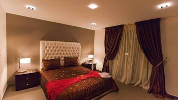 A bedroom with a large bed, two bedside tables with lamps, a headboard, and a window with curtains.