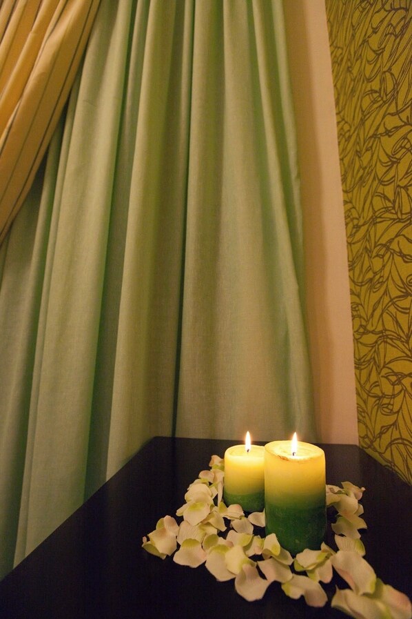 Two candles on a table with a black surface, surrounded by white flower petals. - Sandy Point Villas (Agia Marina)