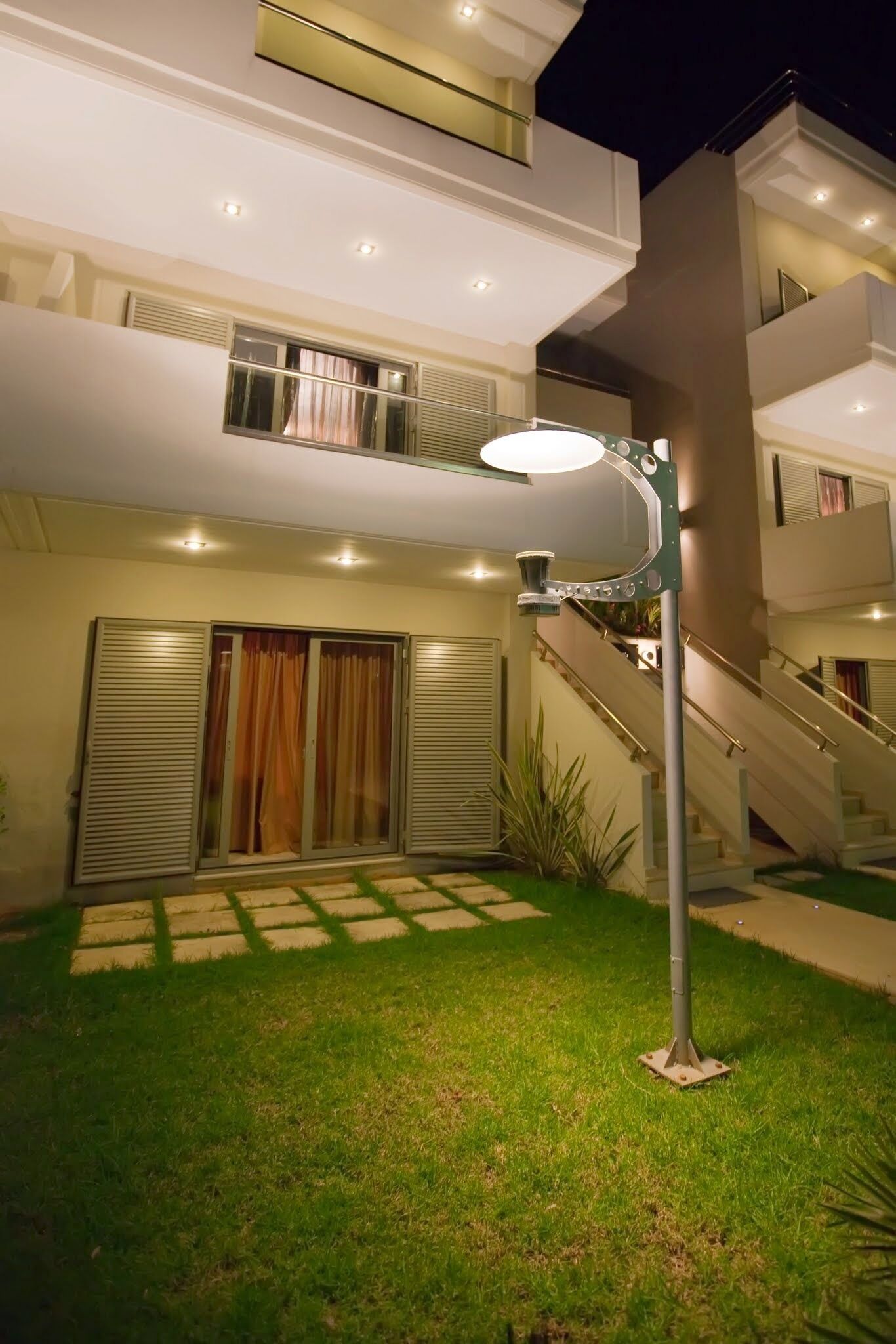 A modern two-story building with a staircase, a covered patio area, and a well-lit outdoor space.