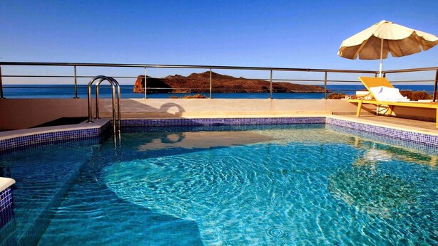 Una piscina azul cristalina con vista al mar y una montaña al fondo.