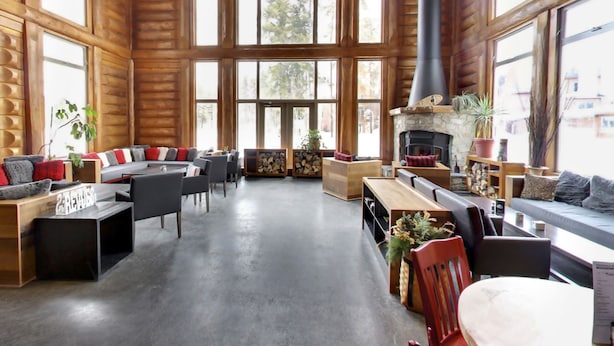 L’intérieur d’une cabane en rondins, avec une cheminée, de grandes fenêtres et un coin salon confortable.