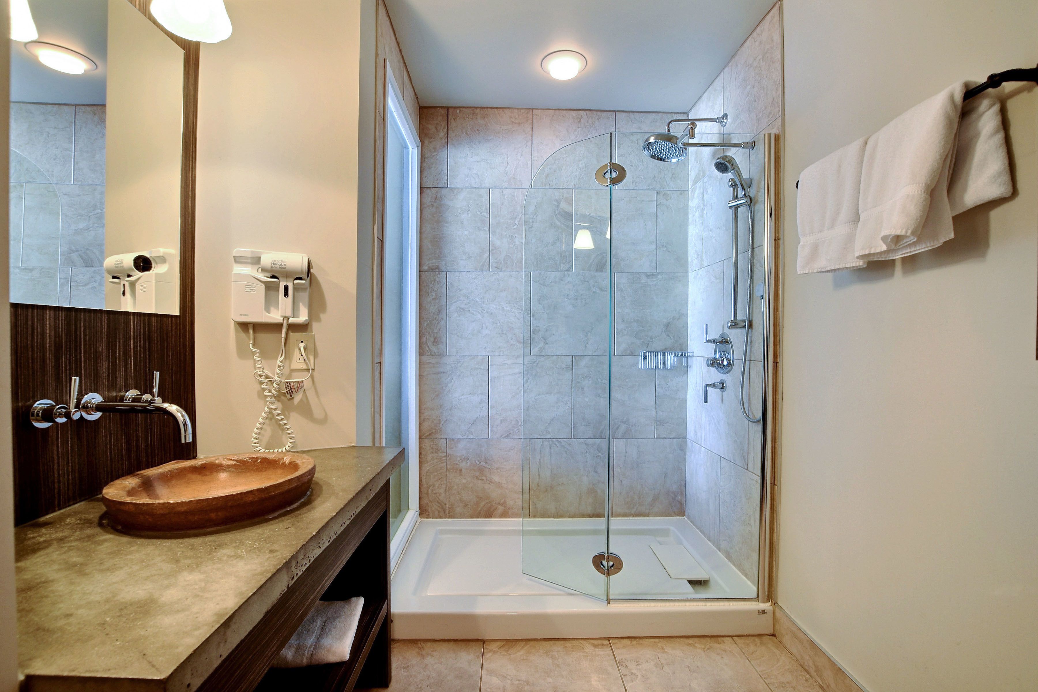 Un baño moderno con ducha envuelta en vidrio, tocador de madera con lavamanos y un espejo.