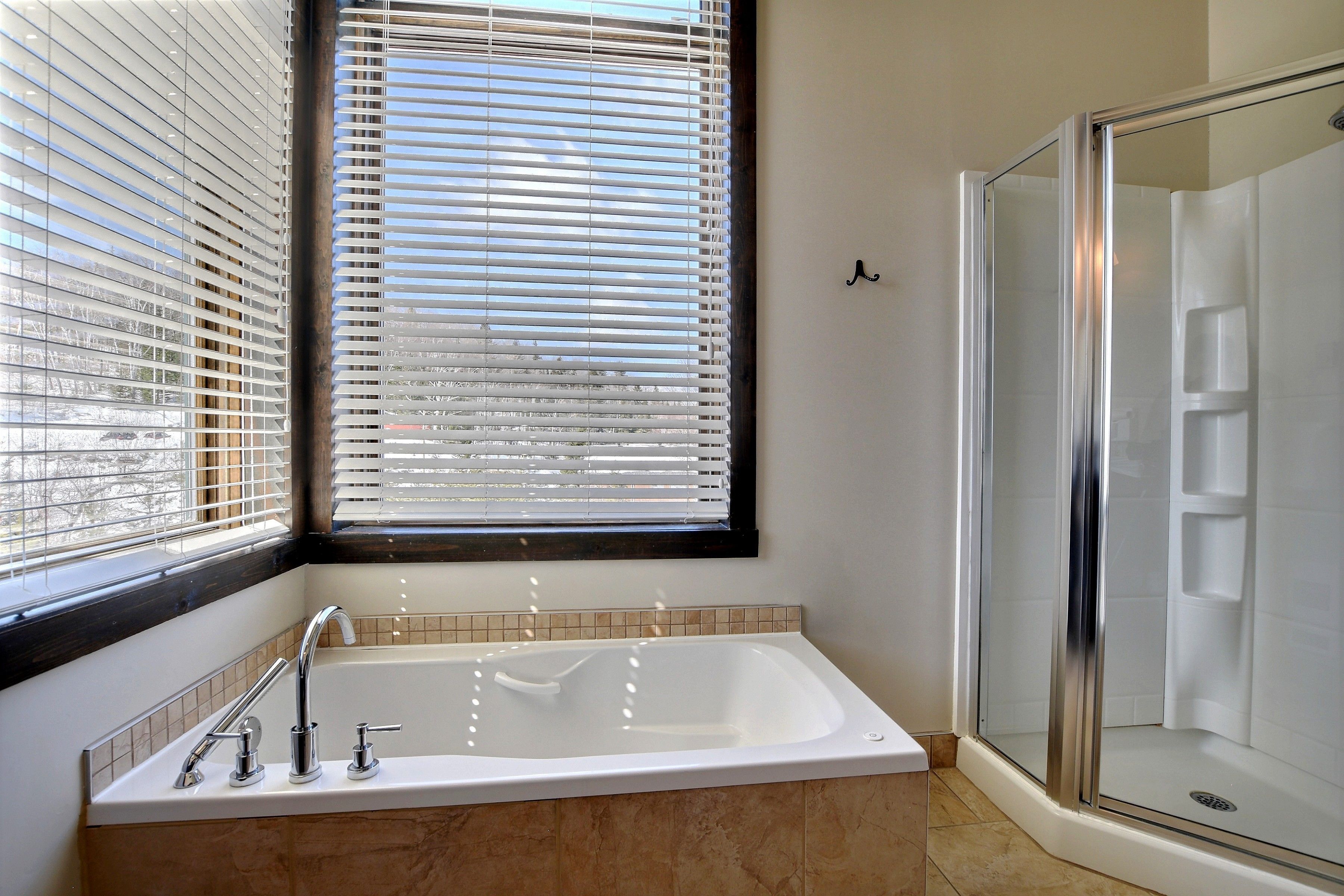 Une salle de bain avec une baignoire, une douche et une fenêtre équipée de stores.