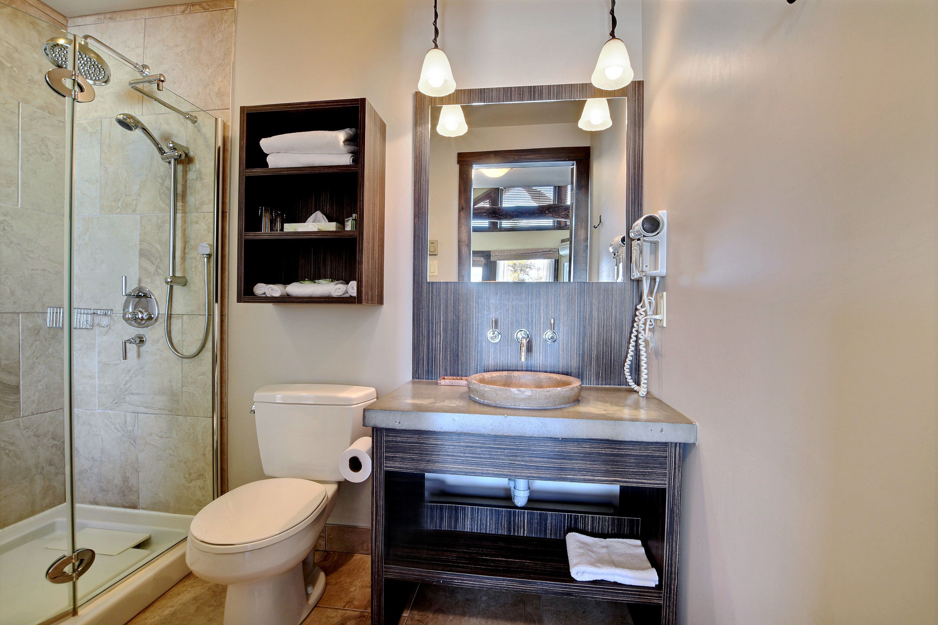 A bathroom with a glass-enclosed shower, a toilet, a sink with a wooden vanity, and a mirror with lights.