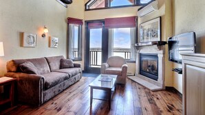 Un salon chaleureux avec une cheminée, un plancher en bois, un canapé, un fauteuil et un téléviseur.