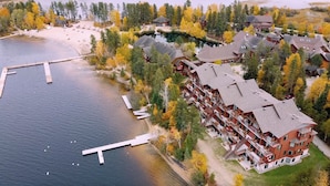 Vue aérienne d’un complexe hôtelier au bord d’un lac, avec un quai, des bâtiments à plusieurs étages et des arbres environnants.