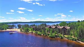 Un chalet au bord du lac, composé de plusieurs bâtiments, avec un quai et une vue dégagée sur le lac et la forêt environnante.