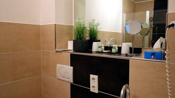 Un bagno con uno specchio, un lavandino, un porta asciugamani e una pianta sul ripiano.