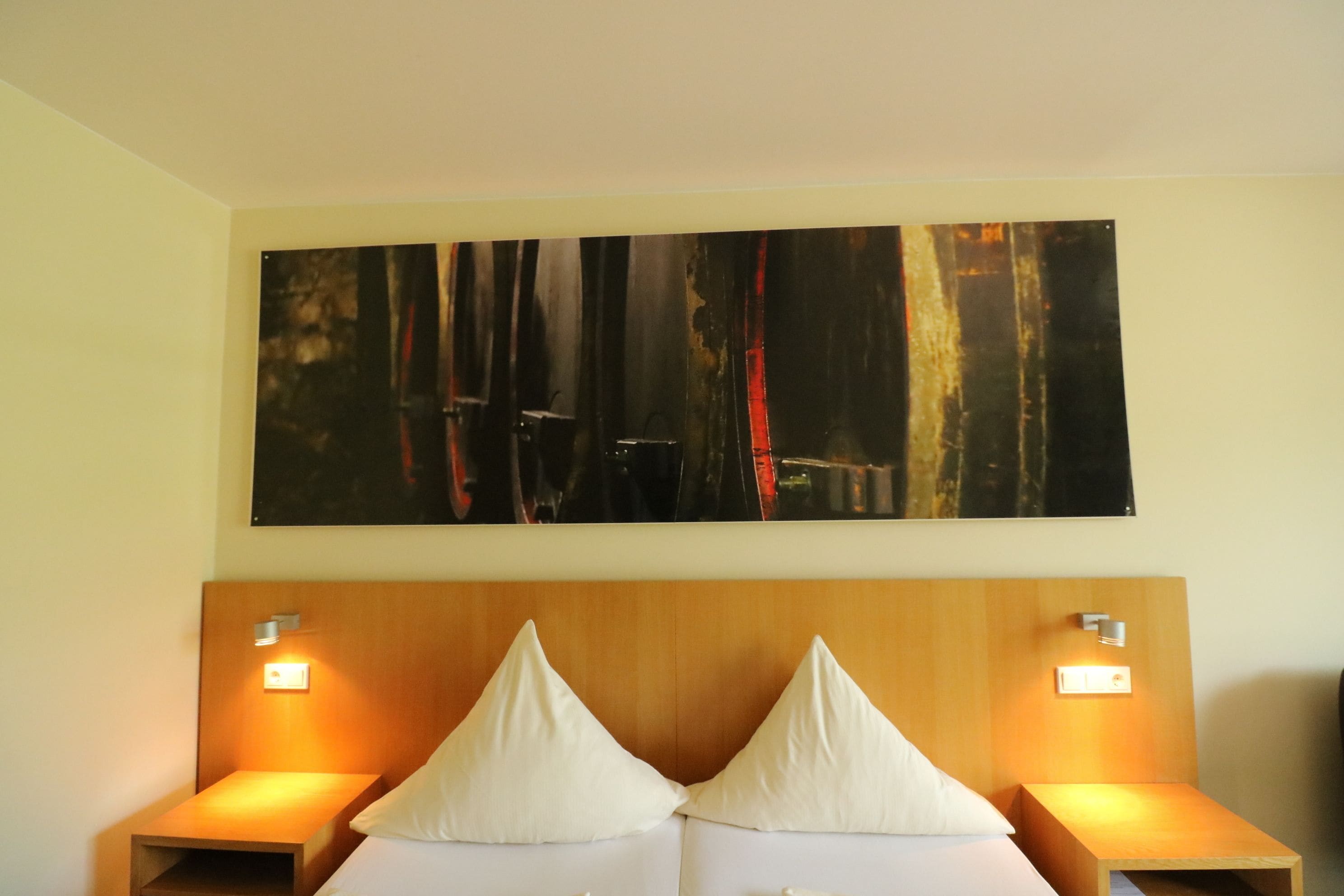 Een hotelkamer met een groot abstract schilderij, een houten hoofdbord en twee bedlampjes.