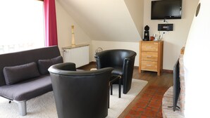 Una sala de estar moderna con un sofá, dos sillones negros, un aparador de madera y un televisor de pantalla plana montado en la pared.