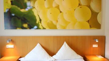 A hotel room with a wooden headboard, two white pillows, and a wall-mounted picture of yellow grapes.