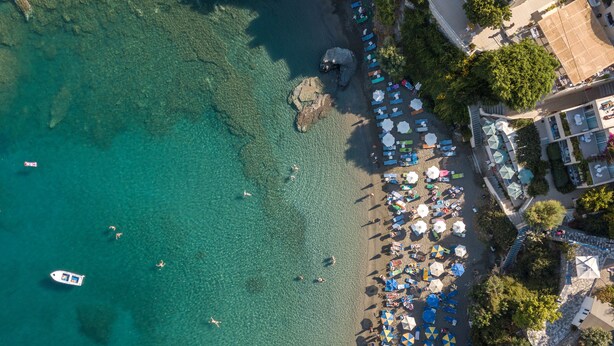 An aerial view of a beach with clear turquoise water, a row of umbrellas, and a boat in the water.
