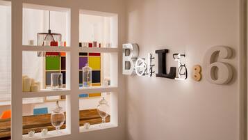 Una habitación con una lámpara de pared que dice "Belt 6" y una ventana con estantes que muestran diversos vasos y velas.