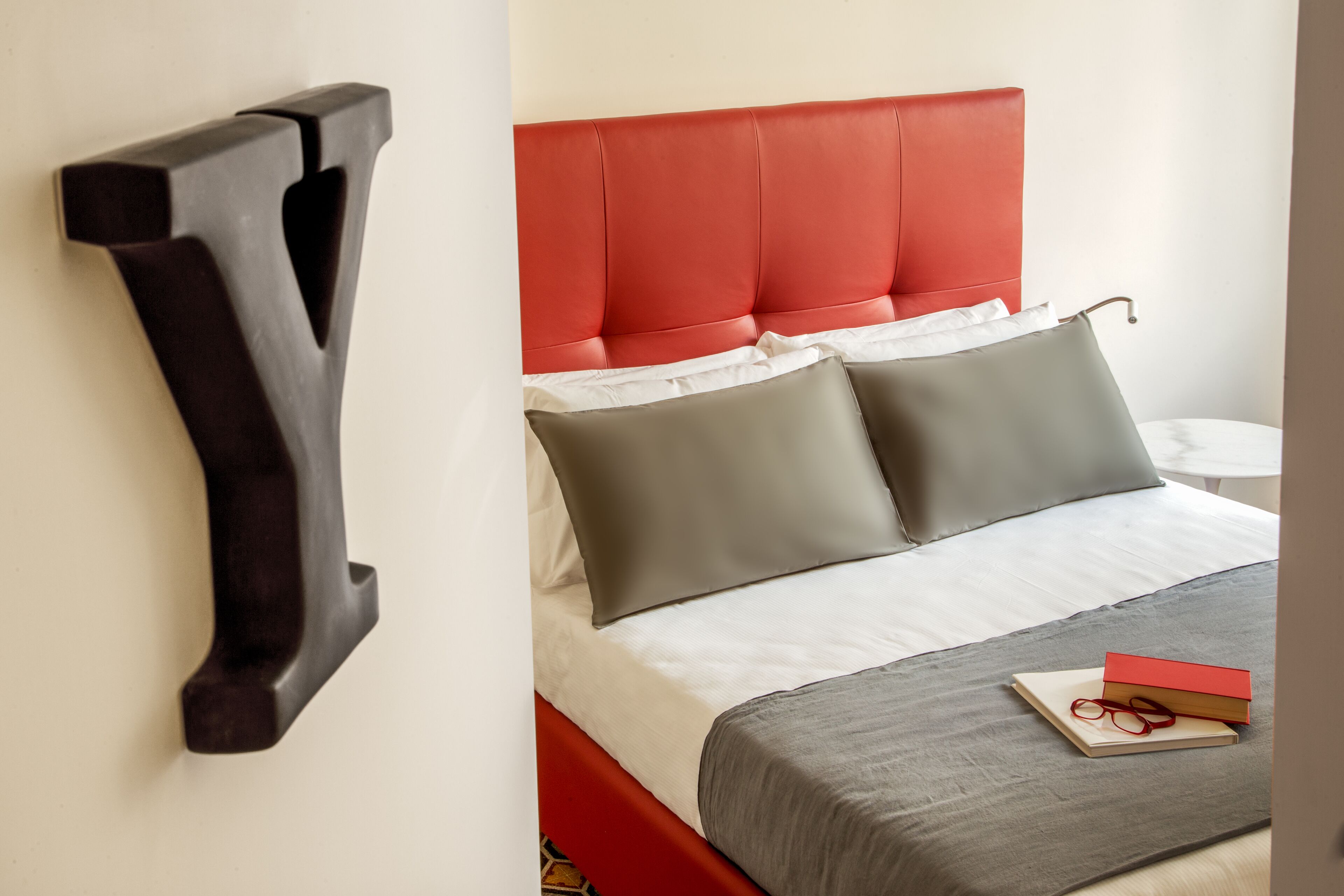 Une chambre d’hôtel moderne avec une tête de lit rouge rembourrée, une couvre-lit grise et un élément décoratif en bois sur le mur.