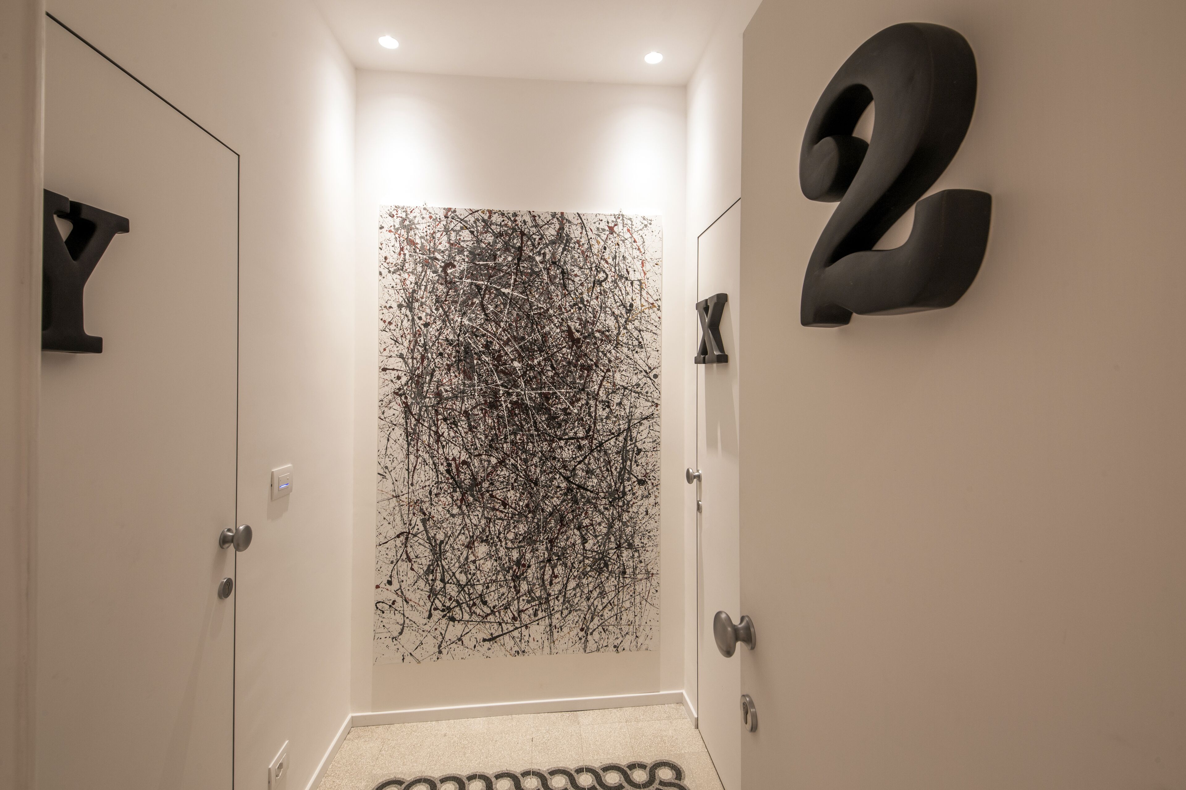 Un pasillo con una obra de arte abstracto moderna en la pared, un letrero con el número '2' y una alfombra estampada en el suelo.