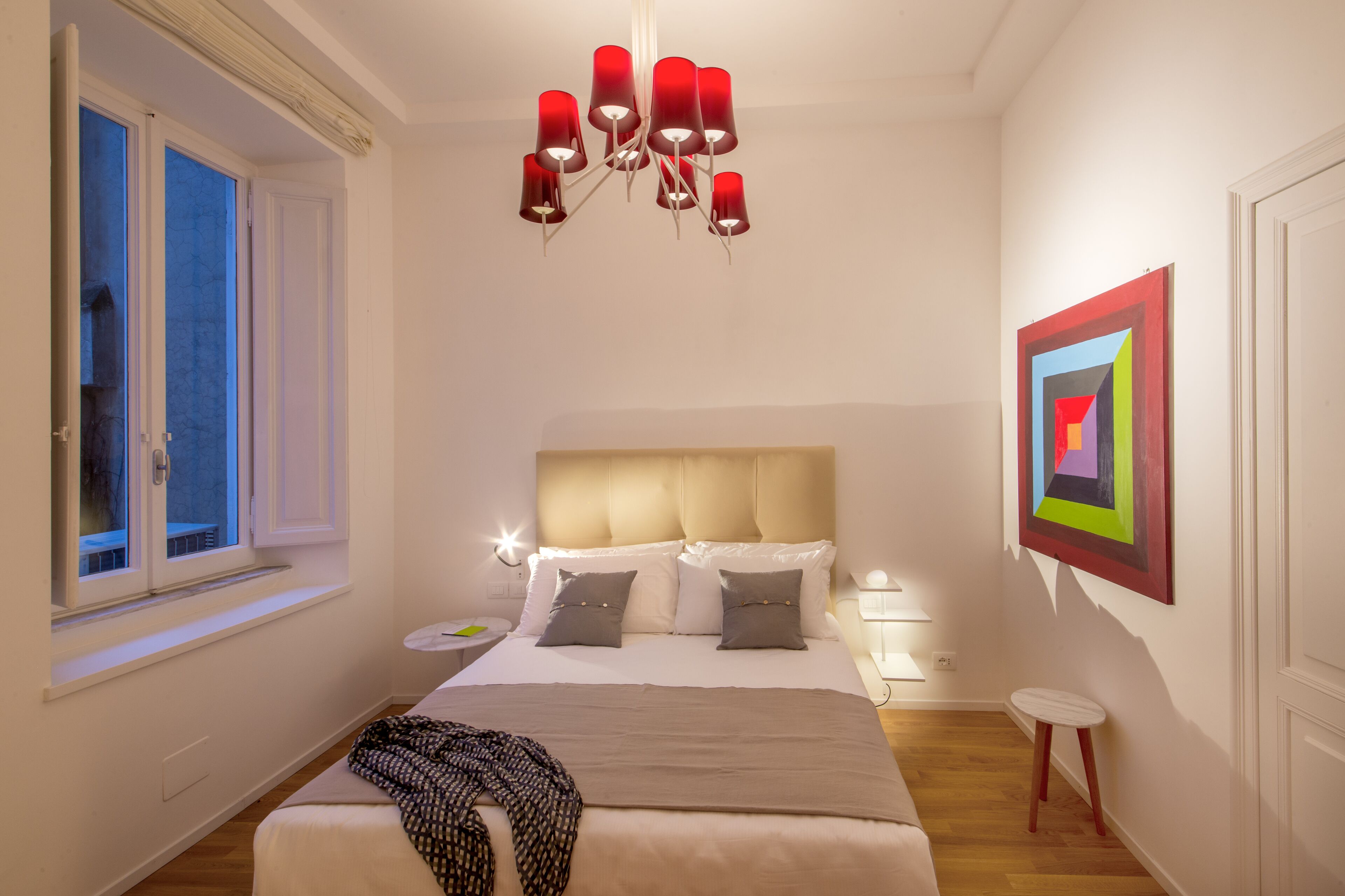 Une chambre à coucher avec un grand lit, un lustre, une fenêtre et un tableau au mur.