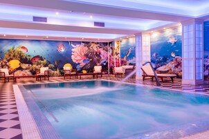 Una amplia piscina interior con suelo a cuadros, rodeada de sillas de descanso y un mural con temática marina.