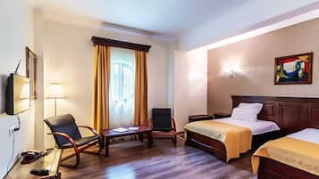Quarto de hotel com duas camas, uma mesa, uma cadeira e uma televisão.