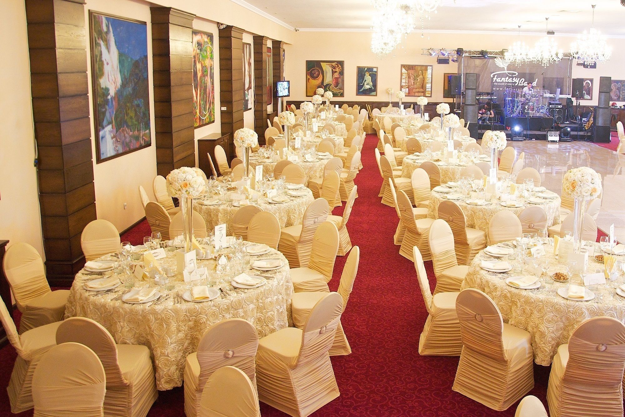 Un salón de banquetes con mesas redondas, sillas blancas y una alfombra roja.