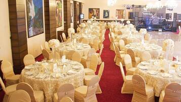 Un salón de banquetes con mesas redondas, sillas blancas y una alfombra roja.