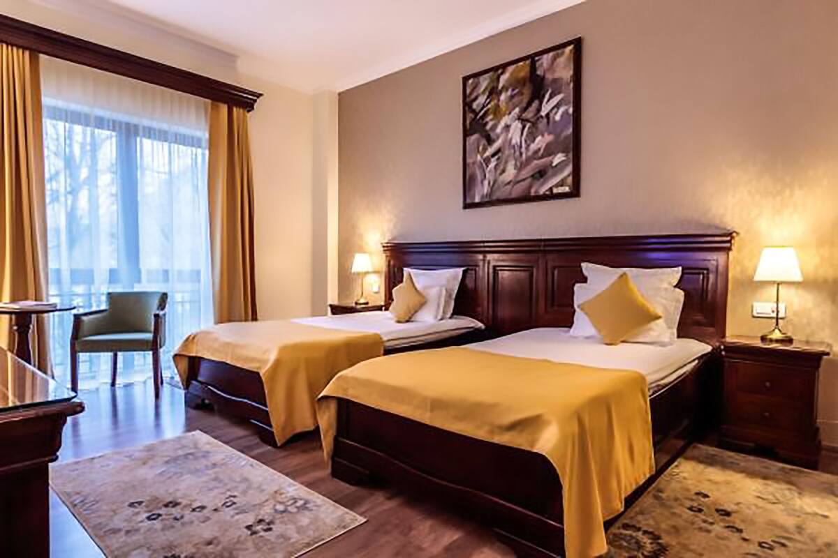 A hotel room with two beds, a chair, a desk, and a window with curtains.