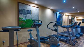 Un gimnasio con cintas de correr, bicicletas estáticas y una máquina de remo.