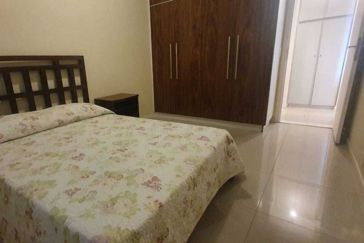Un dormitori amb llit, panell de capçal de fusta, un armari i una petita taula de nit.