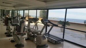 Un gimnasio con máquinas de cardio y una cinta de correr, con vistas a una playa y al océano.