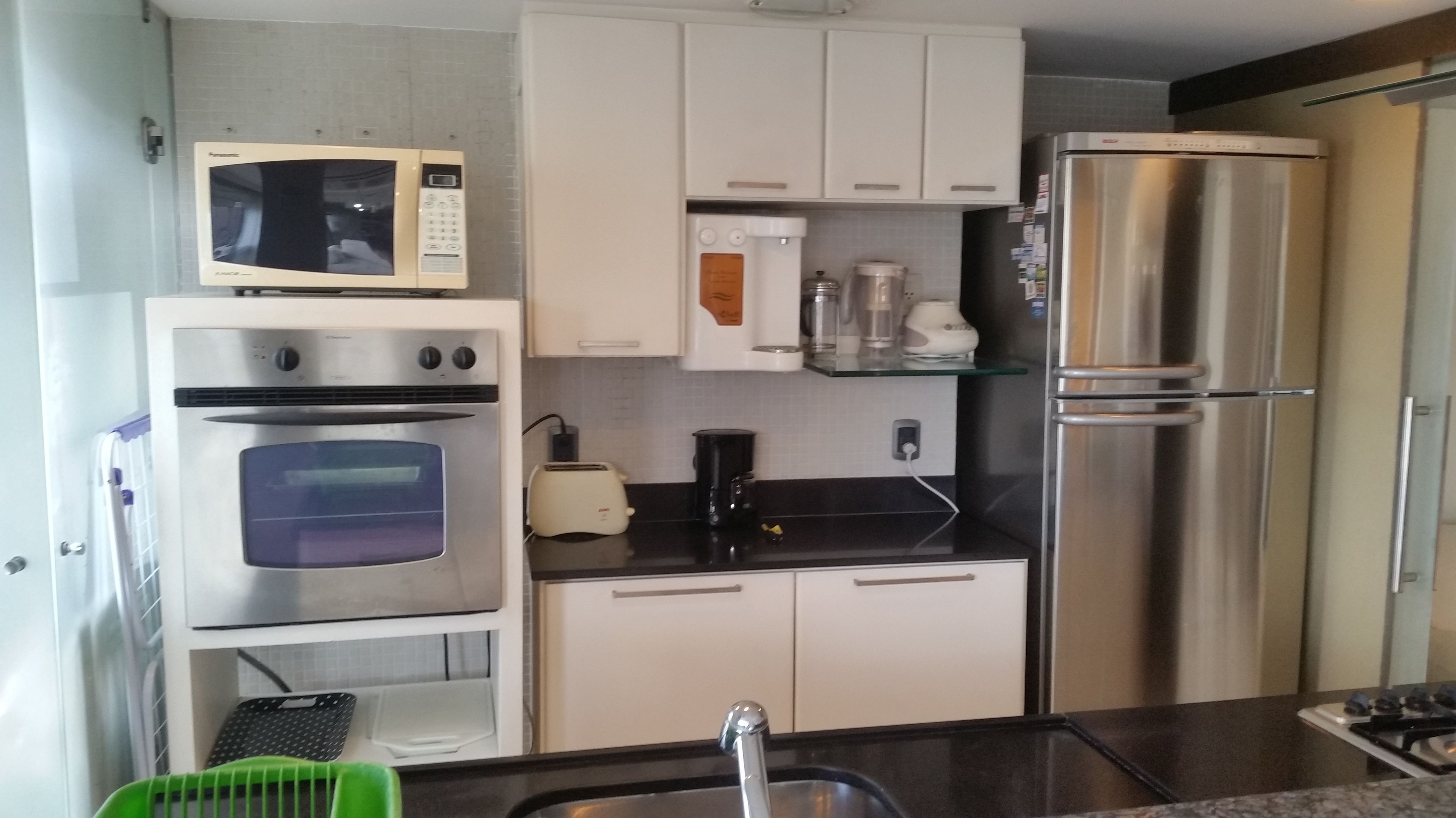 A compact kitchen with a built-in microwave, oven, and stainless steel refrigerator.