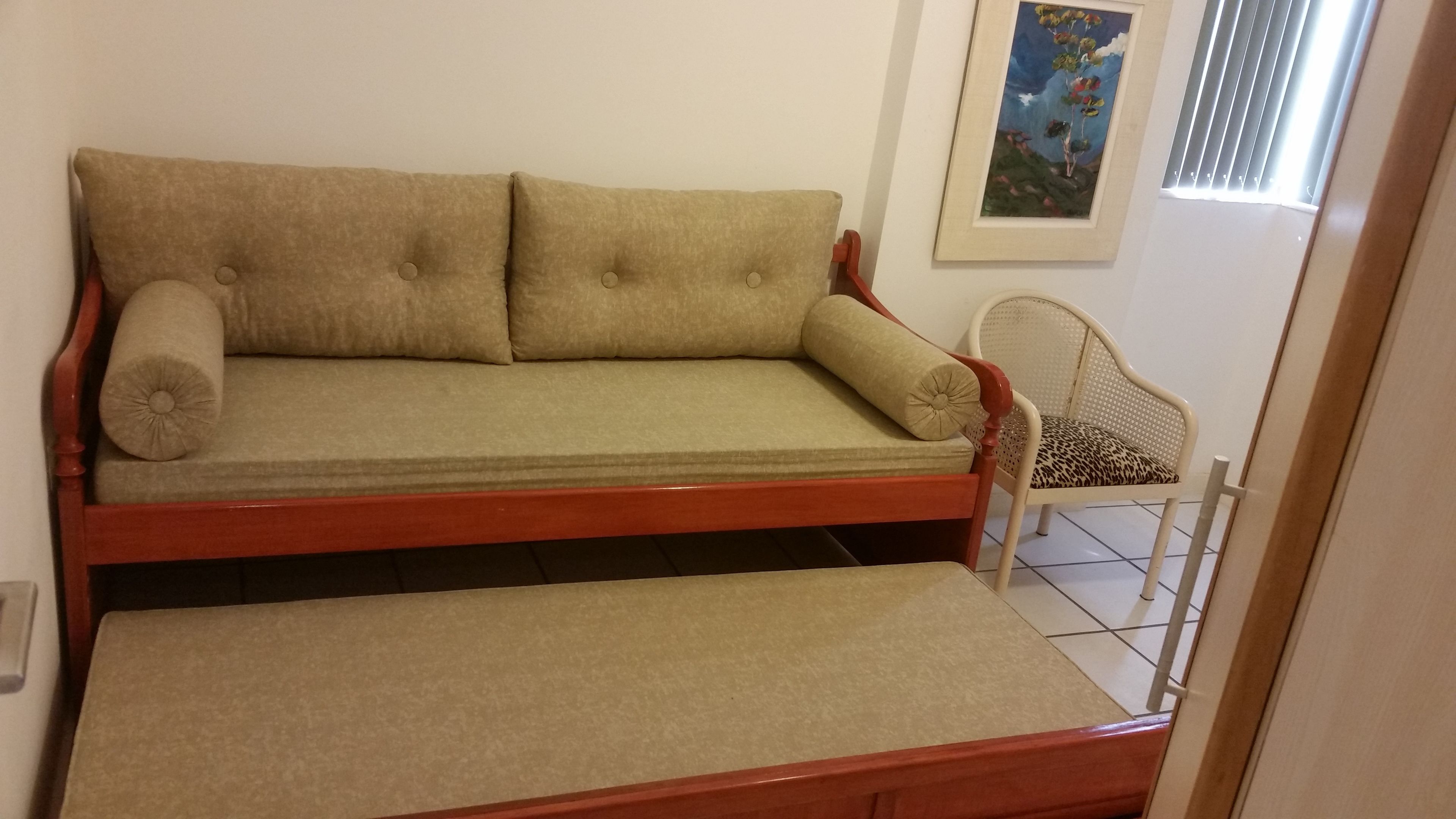Ein Schlafsofa mit Holzrahmen und passender Kissen, ein Sessel mit Leopardenmuster-Kissen und ein Bild an der Wand.