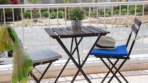 A balcony with a table and chairs, a potted plant, and a view of buildings and greenery. - Paphos Love Nest Apartment (Paphos)