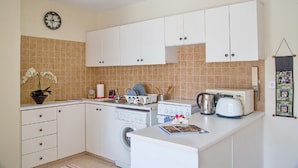 A compact kitchen with white cabinets, a washing machine, a toaster, and a clock on the wall. - Paphos Love Nest Apartment (Paphos)