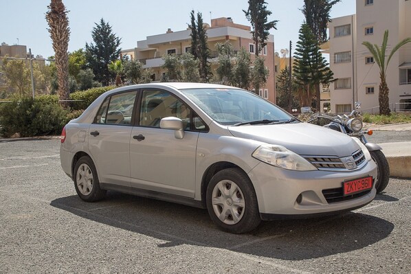 Une voiture à hayon argentée est garée sur un parking, avec des bâtiments et des palmiers en arrière-plan.