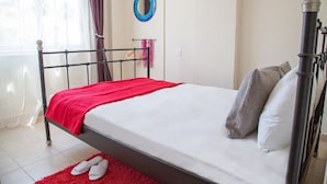 A neatly made bed with a red blanket, pillows, and a pair of slippers on a red rug. - Paphos Love Nest Apartment (Paphos)
