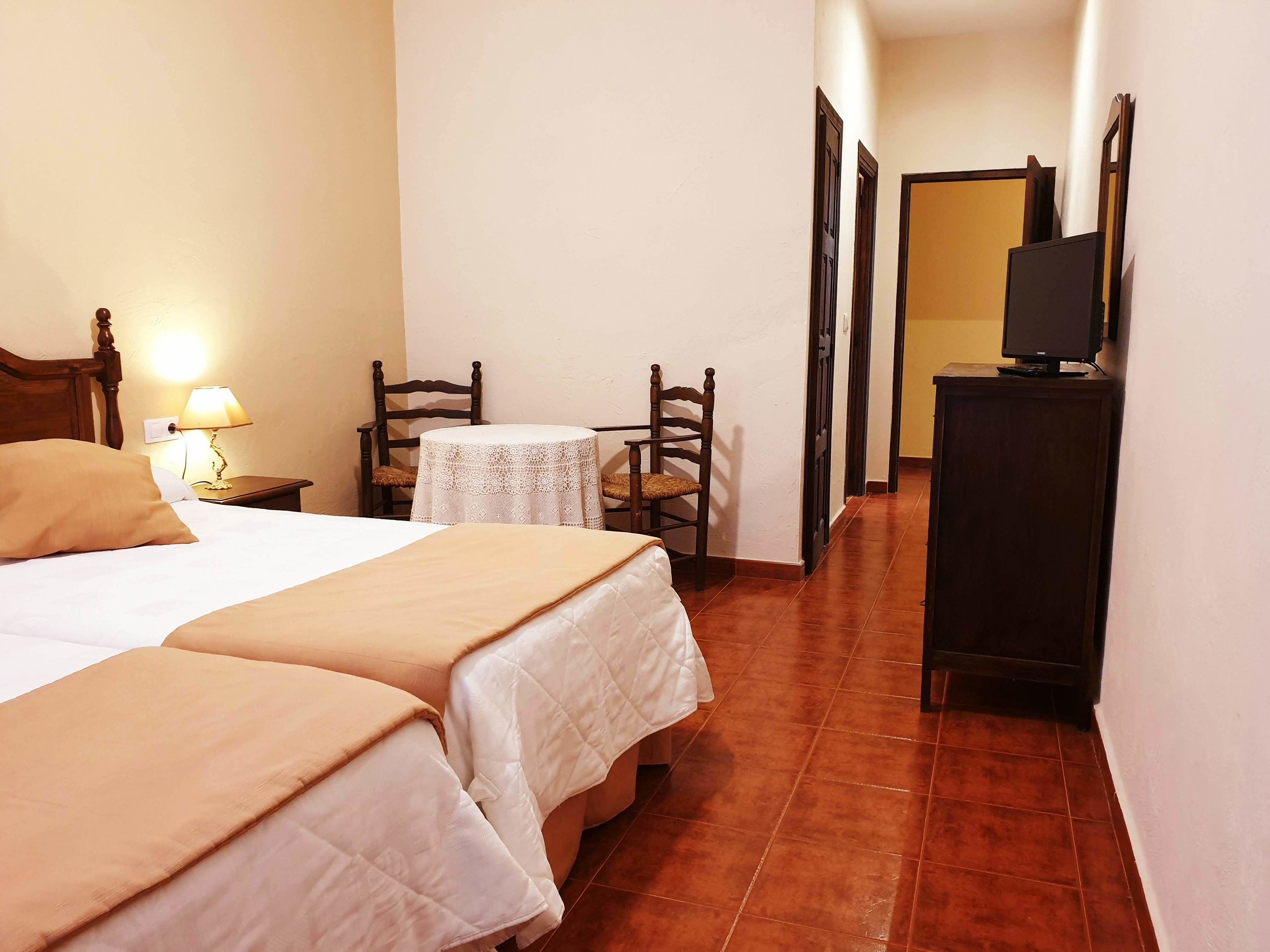 Une chambre d’hôtel avec deux lits, une petite table, une chaise, un téléviseur posé sur un meuble et une lampe sur une table de chevet.