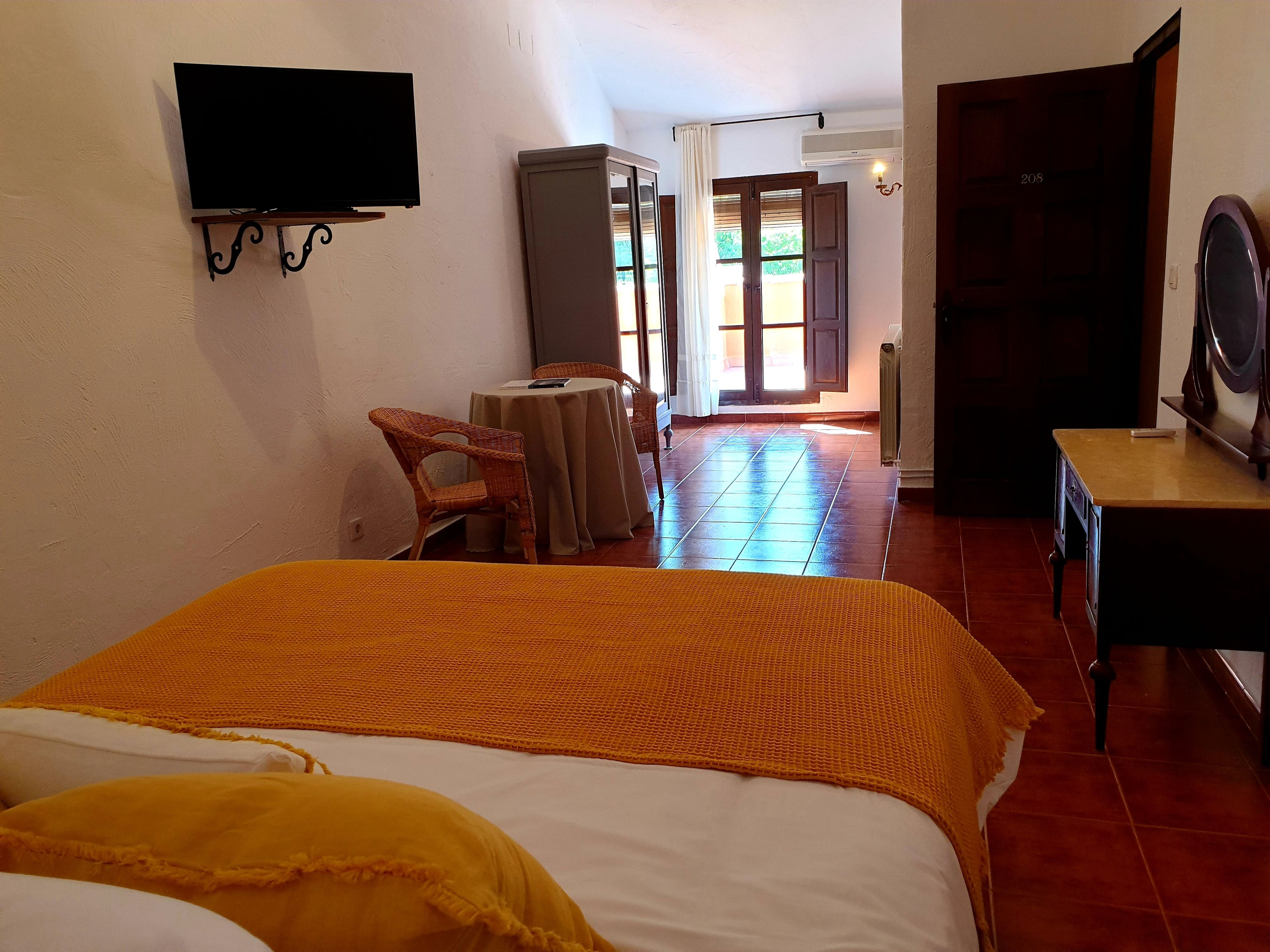 Une chambre d’hôtel avec un lit, un téléviseur fixé au mur, une petite table avec une chaise et une porte donnant sur un balcon.
