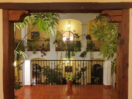 Un espacio interior amplio con una escalera de madera, plantas en macetas y una barandilla decorativa.